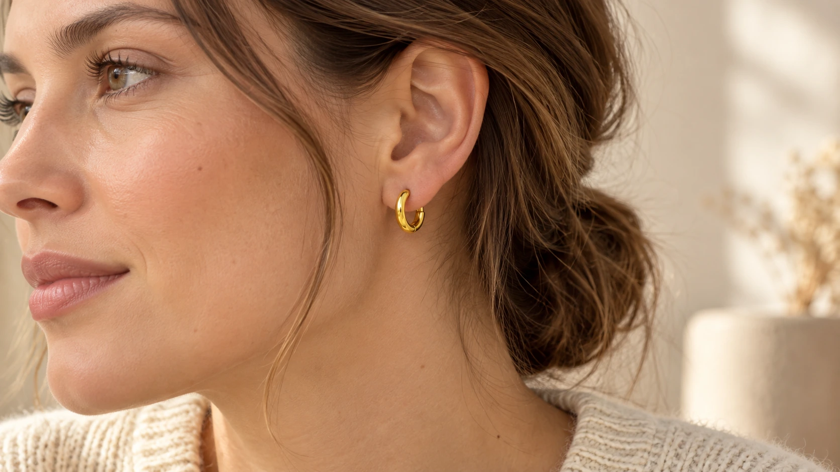 Model met een kleine gouden clipoorbel en een crèmekleurige trui.