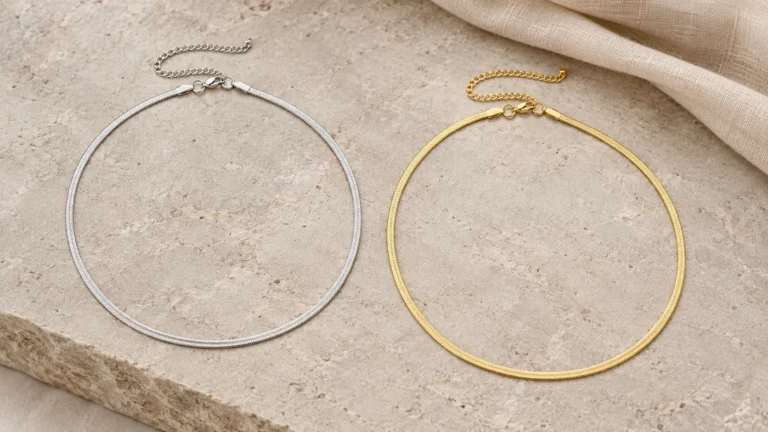 Zilver- en goudkleurige Snake Kettingen naast elkaar op een lichte stenen ondergrond.