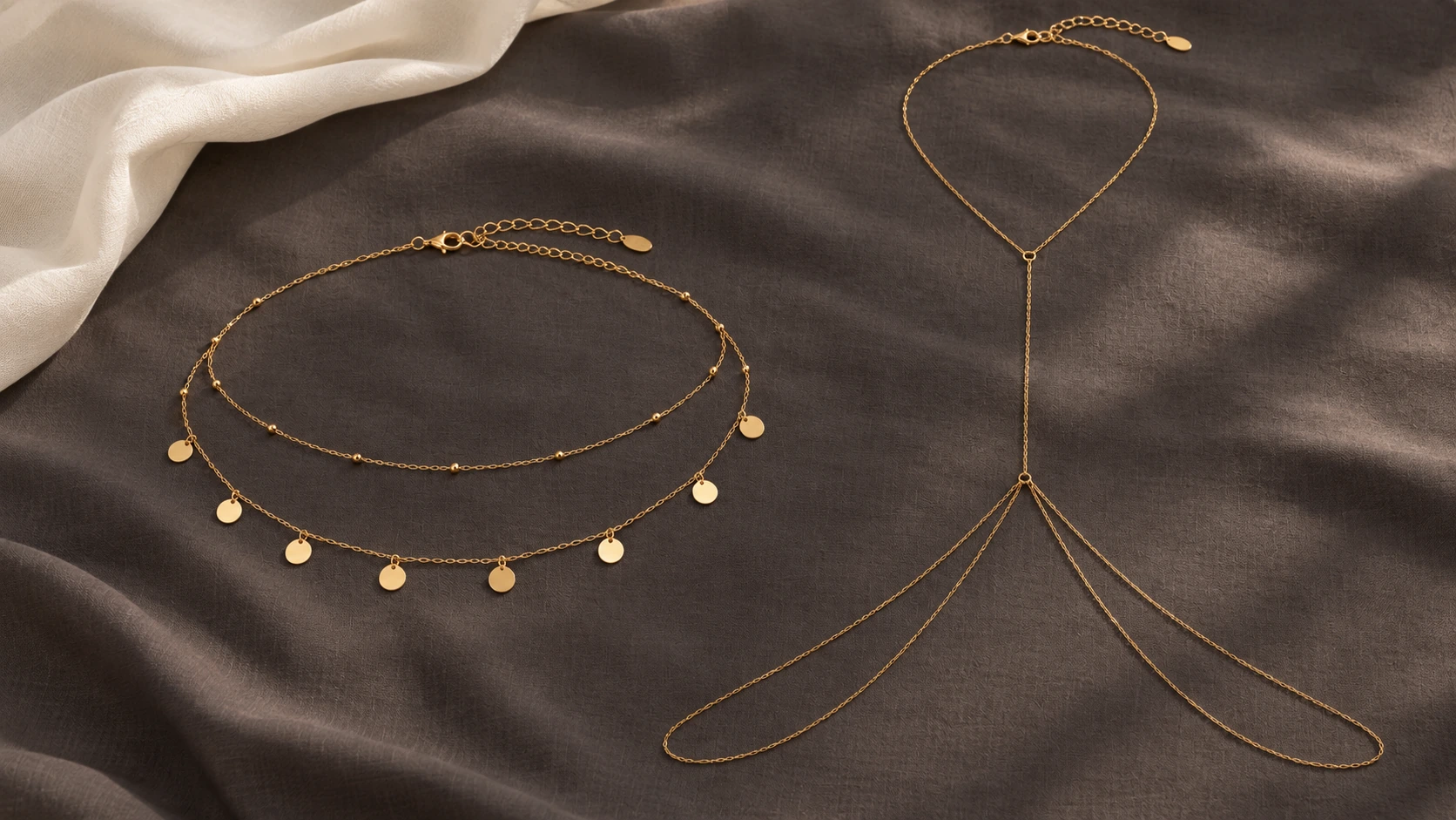 Gouden dubbele buikketting naast een body chain op een donkere stoffen ondergrond.