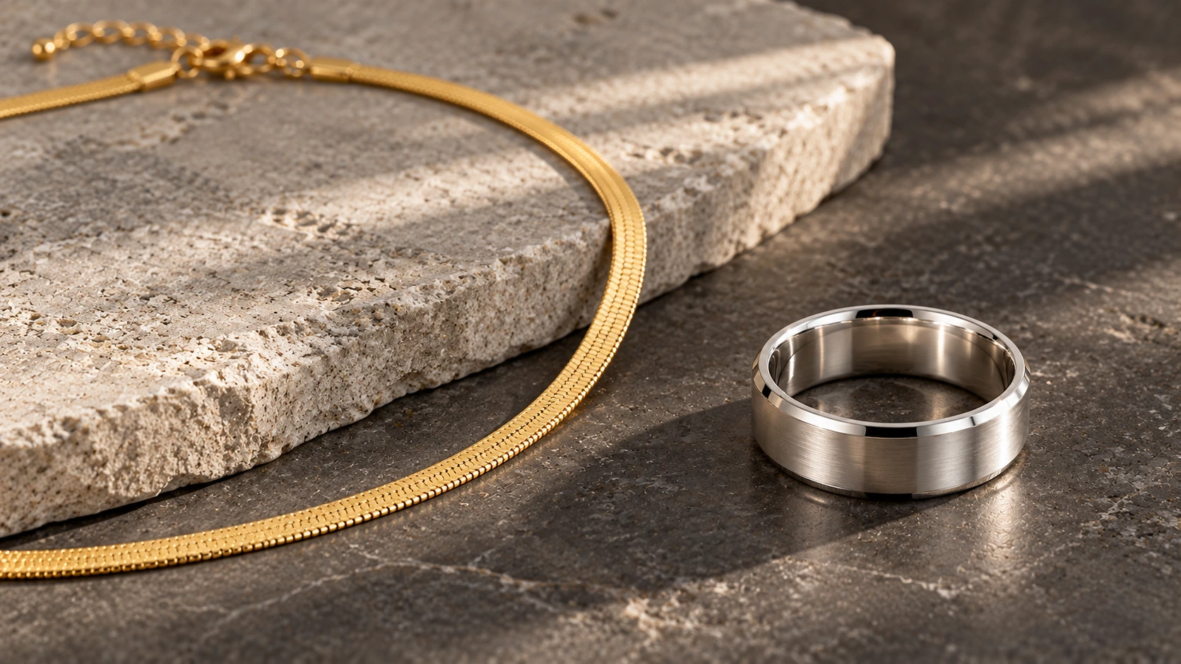 Zilveren ring en gouden Snake Ketting op een matte donkergrijze steen.