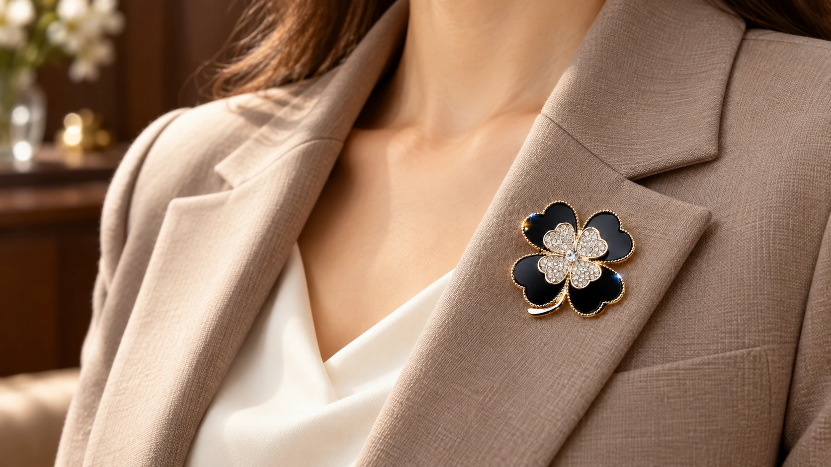 Zwart-gouden klaverbroche op de revers van een taupekleurige blazer.