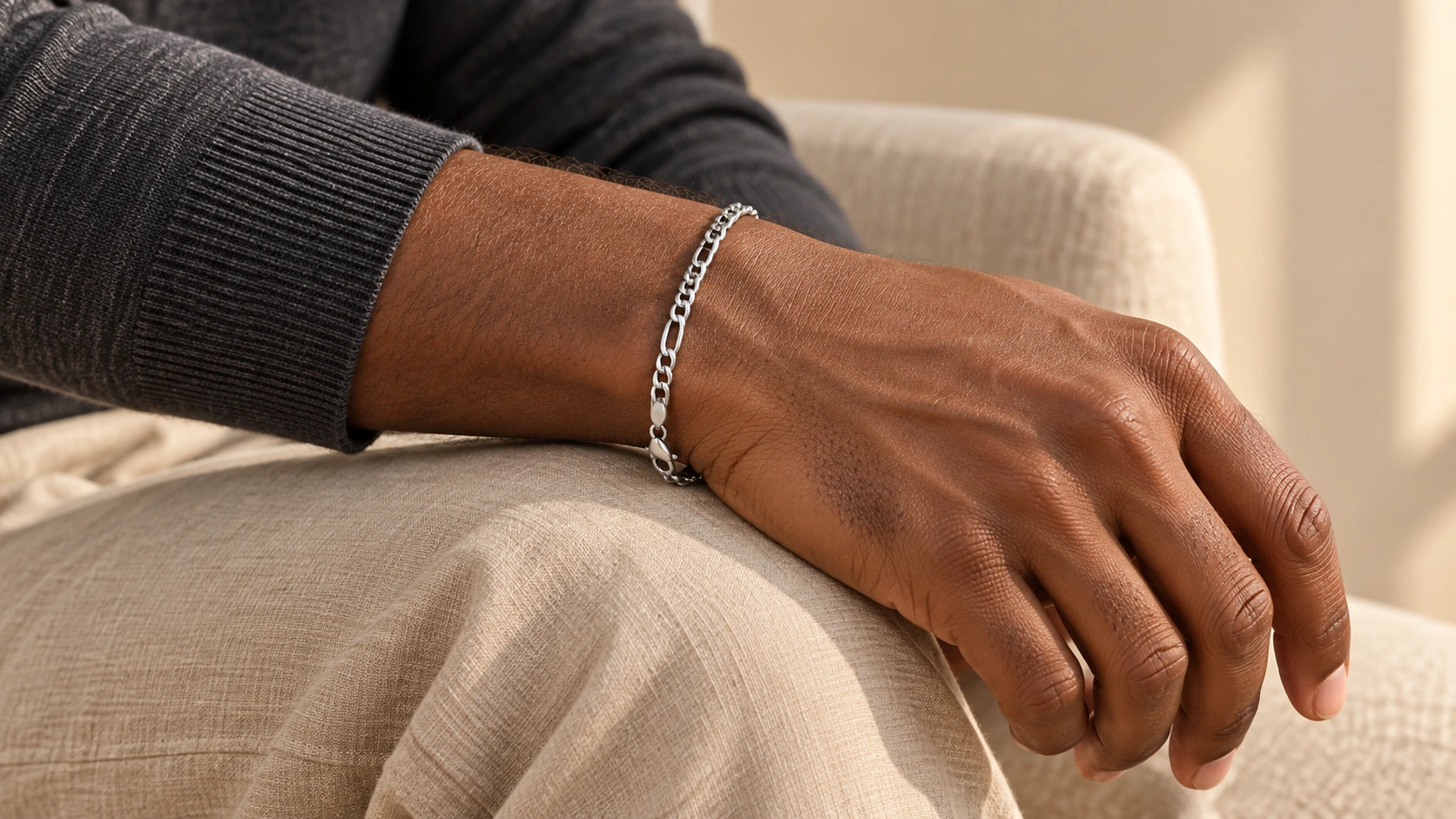 Zilveren Figaro Armband om de pols van een man met een donkergrijze trui.